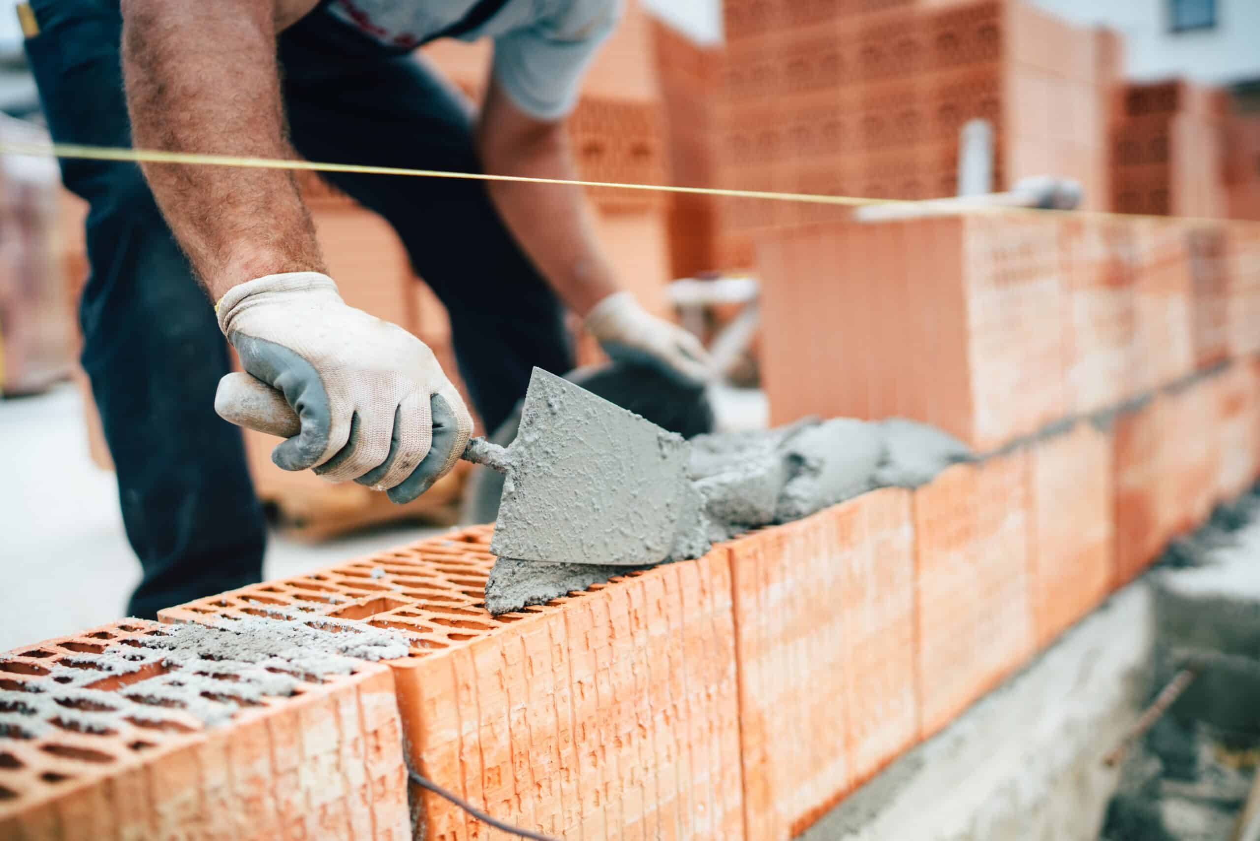 Ouvrier professionnel utilisant une truelle pour construire des murs en briques avec du ciment et du mortier.