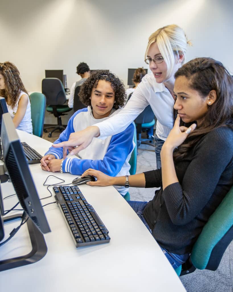 Étudiants adolescents : recherche en ligne. Une enseignante aide ses élèves dans la salle informatique du collège. Image issue d’une série consacrée à l’enseignement secondaire.